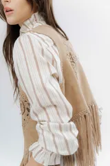 Chaleco negro de estilo boho, confeccionado en semigamuza con detalles de tejido de punto en el frente y la espalda. Presenta un diseño sin mangas con flecos en el ruedo, aportando movimiento y textura a la prenda.