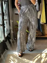 Pantalón gris de pierna ancha con acabado metalizado y bordado de lentejuelas plateadas en patrón vertical, cintura elástica y bolsillos laterales.