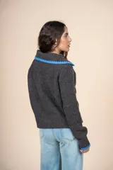 Cardigan de tejido con relieve en color gris oscuro, con cuello camisero y puños en contraste de color azul. Presenta cierre frontal con botones y un calce relajado.