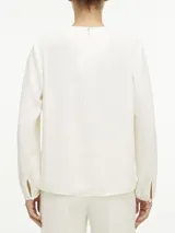 Blusa blanca de poliéster reciclado, con cuello redondo, mangas largas y abertura en el cuello con barra metálica.