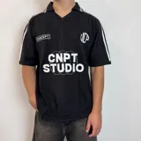 Chomba de tejido de punto color negro, con cuello polo y cierre frontal parcial. Presenta diseño de rayas verticales sutiles en el tejido, detalles de líneas blancas en los hombros y estampado frontal con texto y gráficos en color blanco.