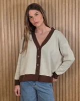 Cardigan de punto color arena con detalles en marrón oscuro en el escote en V, la botonera, los puños y el ruedo. Cuenta con cierre frontal de botones y mangas largas.