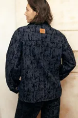 Camisa recta de gabardina con efecto "roto", que aporta volumen y textura. Presenta bolsillos amplios con solapa en el frente adornados con mini estribos dorados y cierre frontal de botones.