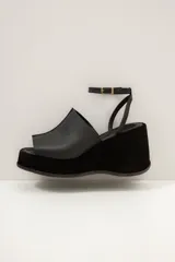 Sandalia de plataforma corrida de cuero marrón, con capellada ancha y tira fina ajustable al tobillo con hebilla metálica.
