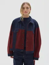 Campera tipo trucker de corte oversize, confeccionada en algodón con diseño colorblock en tonos azul marino y bordó. Presenta cierre frontal con botones metálicos, cuello clásico y bolsillos frontales con solapa.