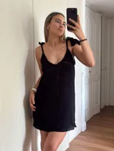 Vestido corto tejido en algodón y lurex, color verde oliva con destellos brillantes. Presenta escote pronunciado en la espalda, breteles con terminación en borlas y diseño calado.