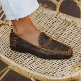 Mocasín de cuero vacuno color marrón envejecido, con punta cuadrada y costuras artesanales de tientos de cuero a contratono en bordes y empeine.