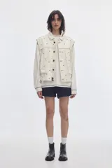 Chaleco oversize de denim color crudo con estampado de lunares negros, cuello camisero, bolsillos delanteros y cierre frontal de botones metálicos.