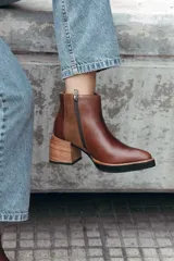 Bota corta de cuero color marrón, con diseño de texturas combinadas en los laterales y elástico. Presenta un taco medio de madera y suela de goma negra.