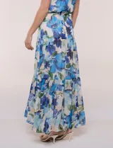 Vestido maxi largo de gasa estampada con diseño floral en tonos azules y verdes sobre base clara, de escote halter y sin mangas. Cuenta con cintura elastizada, lazo de ajuste y falda estructurada en paneles escalonados con forro interno.