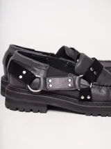 Mocasines de cuero negro con plataforma, diseño tipo náutico con costuras reforzadas en la puntera, detalle de tira sobre el empeine con apliques metálicos y argollas laterales.