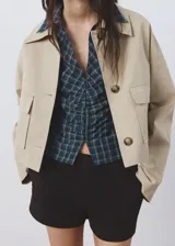 Blusa de algodón con diseño entallado y patrón de cuadros, cuello camisero, manga larga con puños abotonados y cierre frontal de ganchos con detalles fruncidos.