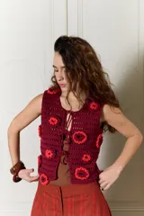 Chaleco tejido en crochet de calce relajado, color bordó con aplicaciones de flores en relieve de color rojo y cierre frontal con lazos.
