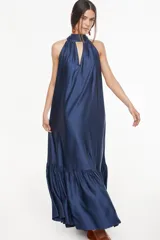 Vestido largo de satén color azul marino, con cuello halter alto y una abertura frontal en forma de lágrima, diseño fluido y amplio con un volante fruncido en el bajo.