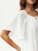 Blusa blanca de manga corta con textura arrugada, escote redondo con abertura en V y lazos ajustables. Presenta detalles de puntilla calada en los hombros.