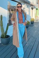 Trench reversible de corte largo, con un lado en color tostado liso y el otro lado con estampado de cuadros. Presenta cuello solapa, cierre frontal de botones, bolsillos laterales y puños con detalle de estampado a cuadros.