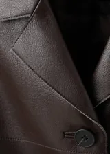 Chaqueta de piel sintética en color marrón, de diseño recto, manga larga y cuello con solapa. Cuenta con cierre frontal de botones, dos bolsillos laterales y forro interior.