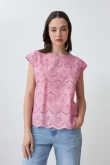 Blusa de algodón color rosa pastel con frente de tela broderie, cuello redondo y mangas cortas con terminación al corte.