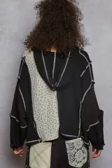 Buzo cropped de manga larga, color negro, con cuello tipo polo y cierre parcial de botones. Presenta un diseño de patchwork con paneles de tejido acanalado negro y un panel central de tela estampada con microflores blancas, todo unido con costuras expuestas en hilo blanco.