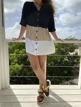 Vestido corto camisero con bloques de color: negro en la parte superior, beige en el medio y blanco en la parte inferior. Tiene cuello en V y cierre frontal con botones de madera.