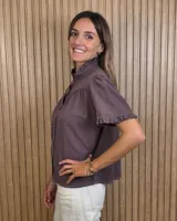 Camisa de manga corta color beige, con cuello alto con volados, botonadura frontal y mangas abullonadas con terminación fruncida.