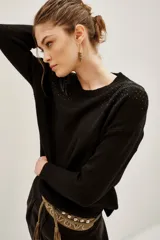 Sweater negro de punto con cuello redondo, manga larga y detalle de tachas metálicas en los hombros formando un diseño de rayo.