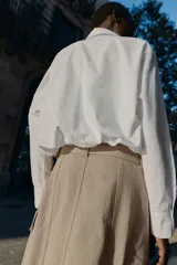 Camisa de popelín color blanco, con cuello solapa, manga larga y bajo abullonado con elástico interior. Cierre frontal con botones.