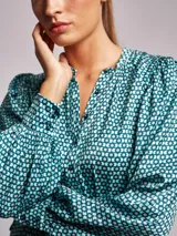 Vestido midi de tela satinada con estampado geométrico en tonos verdes y violetas. Presenta cuello mao, cierre frontal con botones y mangas largas abullonadas con puños abotonados.