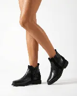 Bota corta tipo chelsea de cuero negro, con paneles laterales de gamuza y suela plana de goma. Presenta un diseño minimalista con tirador en la parte trasera.