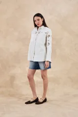 Sobrecamisa blanca de algodón con bordados florales calados en mangas, cuello y pechera. Corte oversize, manga larga y dos bolsillos frontales.