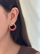 Aro de metal dorado, tipo argolla gruesa, con pequeñas cuentas facetadas de color coral/rojo engarzadas en la parte inferior.