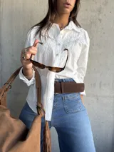 Camisa blanca de corte clásico con sutiles rayas verticales y delicado bordado floral en la parte superior delantera. Presenta cuello camisero, cierre frontal con botones y mangas largas.