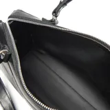 Cartera estilo baúl de cuero negro con doble asa de mano, correa ajustable y extraíble, y placa metálica con logo en el frente.