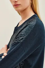 Sweater de punto en color azul oscuro, con cuello redondo y mangas largas. Presenta un diseño frontal completamente cubierto de lentejuelas brillantes en tonos azulados y verdosos.