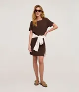 Vestido corto marrón oscuro, estilo camiseta, con escote redondo, mangas cortas y bolsillos laterales. El bajo es redondeado.