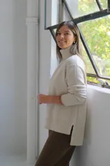 Sweater de punto color crudo con cuello alto, manga larga y detalle de costura vertical central. Presenta puños y ruedo acanalados.