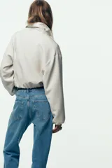 Chaqueta bomber negra con cuello solapa, manga larga abullonada y puños elásticos. Presenta falsos bolsillos de doble vivo en la parte delantera y cierre frontal con cremallera.