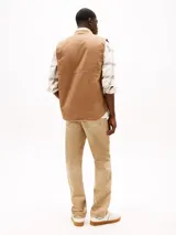 Chaleco de lona color marrón claro con capucha, cierre frontal con cremallera, dos bolsillos delanteros ribeteados, un bolsillo interior y parche con logo de Tommy Jeans en el pecho.