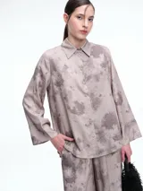 Camisa oversize de lyocell con estampado orgánico efecto lavado. Presenta cuello clásico, cierre frontal con botones, mangas amplias con puños anchos y un diseño de corte relajado con ruedo asimétrico, siendo más largo en la parte posterior.