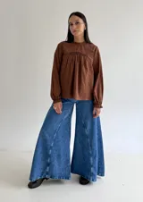 Blusa blanca de corte holgado con cuello redondo, mangas largas con puños elásticos y detalles de puntillas verticales en el frente.