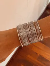 Brazalete rígido compuesto por múltiples aros finos plateados que forman una pulsera ancha.