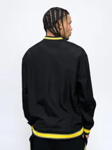 Buzo negro de nylon con cuello en V, puños y pretina con detalles en amarillo y gris. Estampado frontal con la palabra "Peñarol" en amarillo y escudo del club en la manga. Corte clásico.