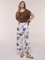 Pantalón crop de lino y rayón, con diseño wide leg de corte holgado, estampado tropical de hojas en tonos verde, azul y marrón sobre fondo blanco. Cuenta con pretina trasera elastizada y bolsillos delanteros.
