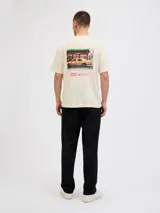 Camiseta de manga corta y cuello redondo, color blanco antiguo (off-white), con un estampado gráfico grande en la espalda que simula una fotografía urbana nocturna con un taxi amarillo y texto en tipografía cursiva y recta.