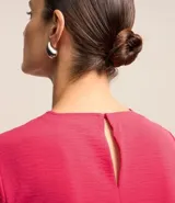 Blusa blanca de poliéster con cuello redondo, mangas cortas, cierre trasero en forma de gota, pequeñas aberturas laterales y acabados en pespuntes en las mangas y el cuello.