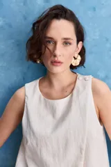 Top blanco sin mangas, con cuello redondo, diseño cruzado en el frente y cierre con botones en el hombro.