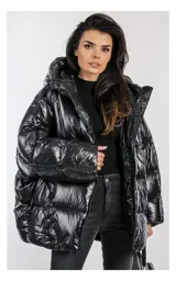 Campera oversize negra con capucha, confeccionada en nailon brillante. Cuenta con bolsillos laterales con cremallera, relleno natural y ajuste inferior con cordón. Presenta cierre frontal con cremallera de doble cursor, detalles de cremalleras con logotipo y diseño acolchado.