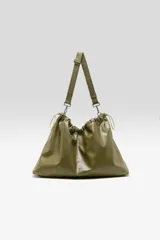 Bolso tipo hobo confeccionado en cuero vacuno color verde militar, con diseño fruncido en la parte superior y cierre con cordón ajustable. Cuenta con una correa larga regulable y desmontable sujeta por mosquetones metálicos.