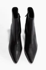 Botines de cuero negro con caña elástica, punta fina y taco fino de altura media.