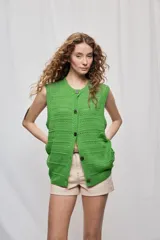 Chaleco de punto sin mangas, de color verde, con escote redondo y cierre frontal con botones. Presenta un diseño calado de silueta amplia.